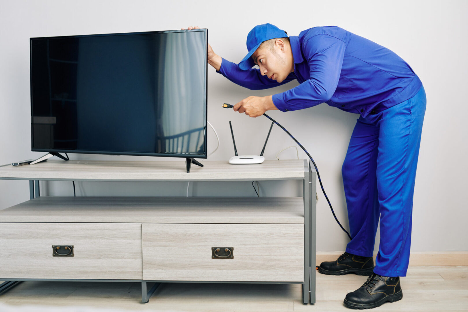 Serious young Vietnamese repairman installing tv set in apartment of customer